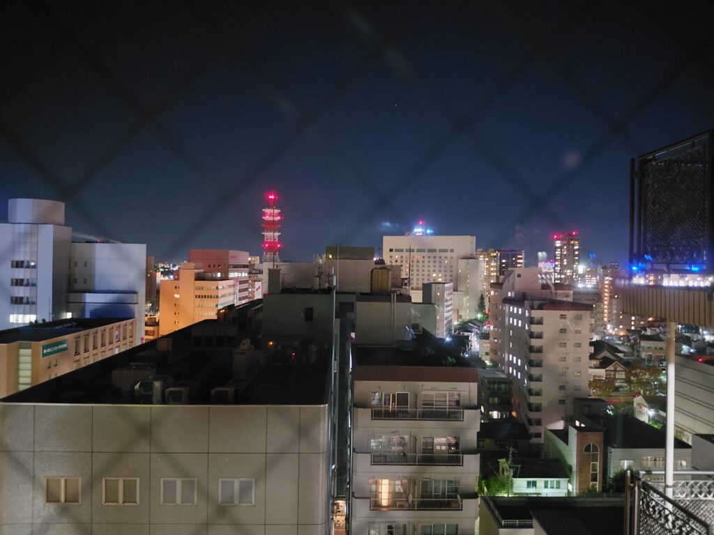 14階の窓から撮影した夜景。手すりが見え、ガラスに室内の光がわずかに映り込んでいる。