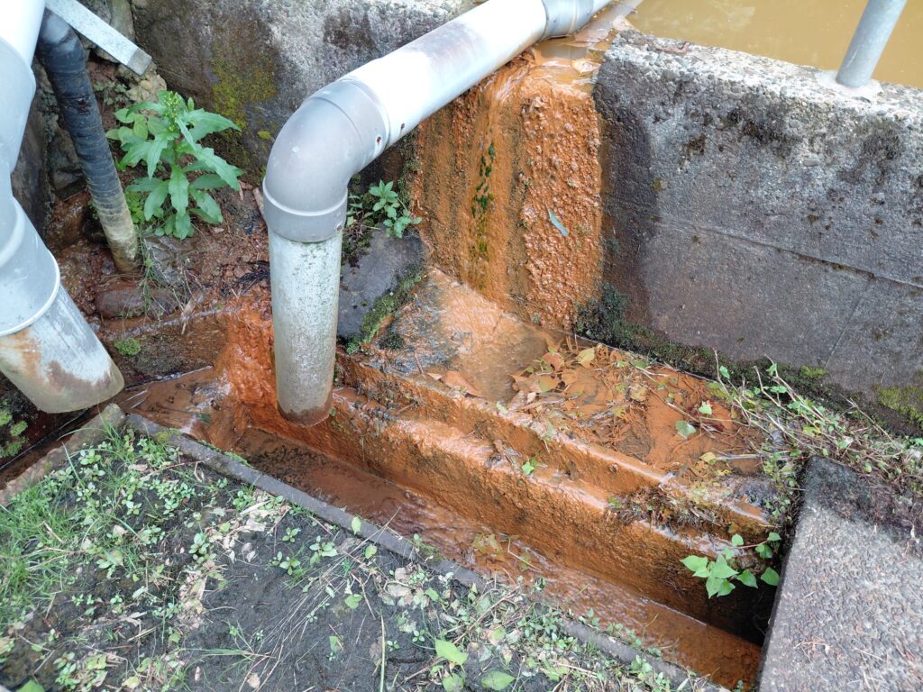防火水槽からあふれ出す茶色い湧水