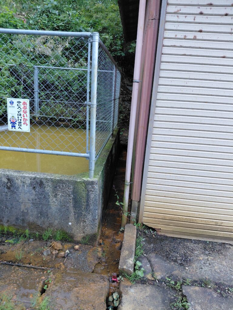 防火水槽と車庫のわずかなすき間を流れる湧水の様子。