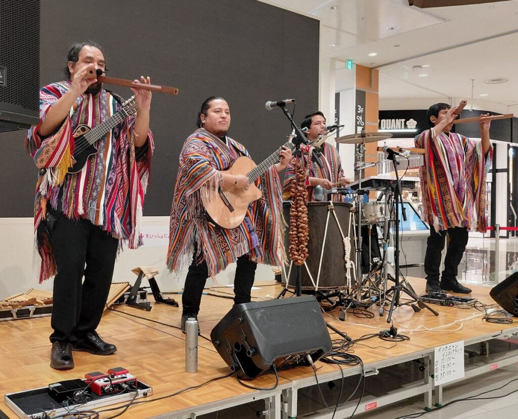 民族衣装をまとった4人組がステージでアンデス音楽を演奏する様子。ケーナやギター、打楽器が響くインカニャンのライブ。