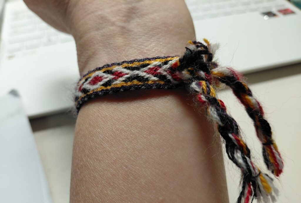 手首に巻いたカラフルなミサンガ。黒・白・赤・黄の糸が編み込まれ、アンデス音楽の思い出とともに手作りの温もりを感じる。