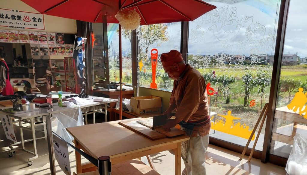 そば職人が包丁で細く麺を切る工程。まな板の上に整然と並ぶそば