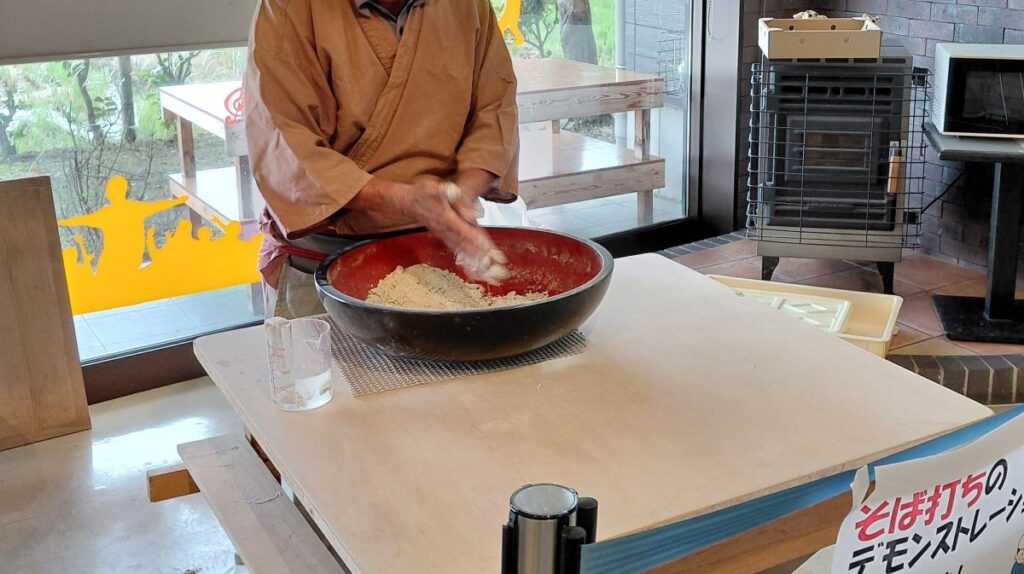 大きな鉢でそば粉に水を加え、手でこね始める様子。いわむろや館内のそば打ちデモンストレーション。